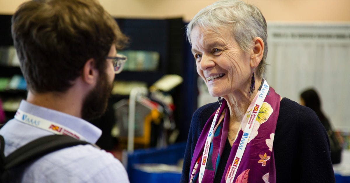 Dr. Lisa Graumlich speaking directly with a young adult male, around college age, at an event.