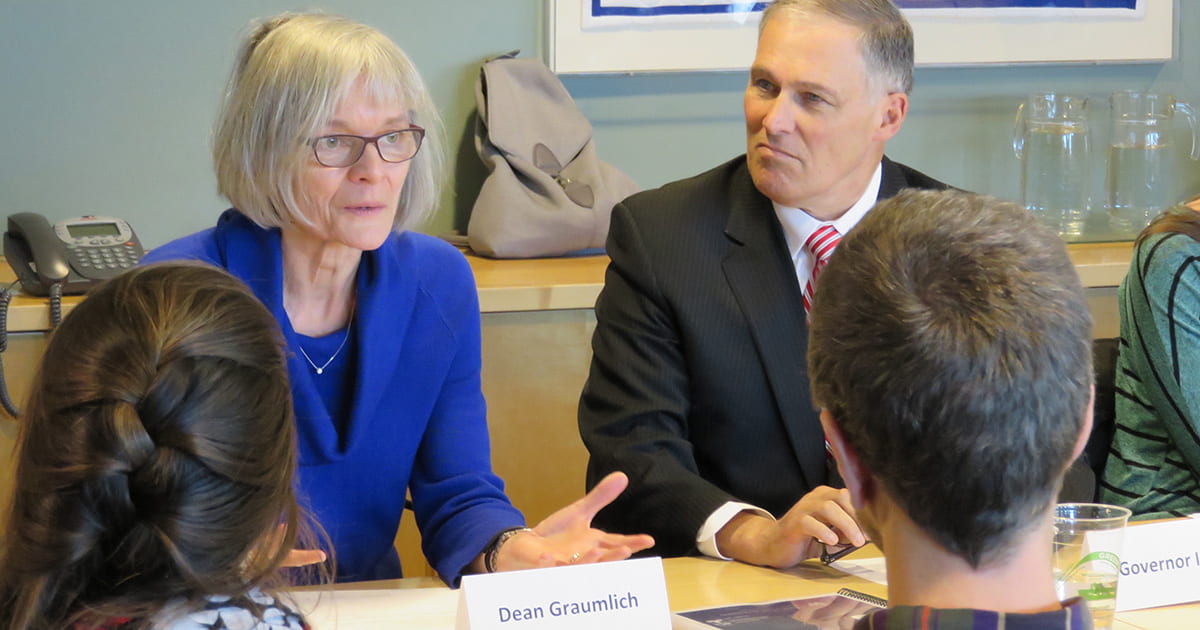 Dr. Lisa Graumlich speaking at a table while setting next to Washington State Governor Jay Inslee.
