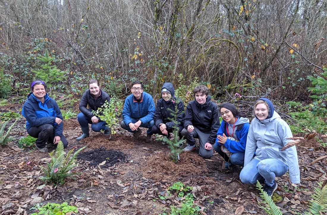 Seven people kneeling in a forested area for a group photo.