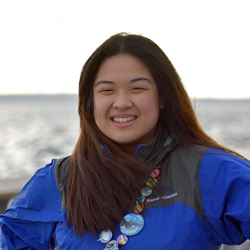 Samantha-Lynn Martinez smiling, wearing a Seattle Aquarium jacket with buttons attached in support of ocean conservation.
