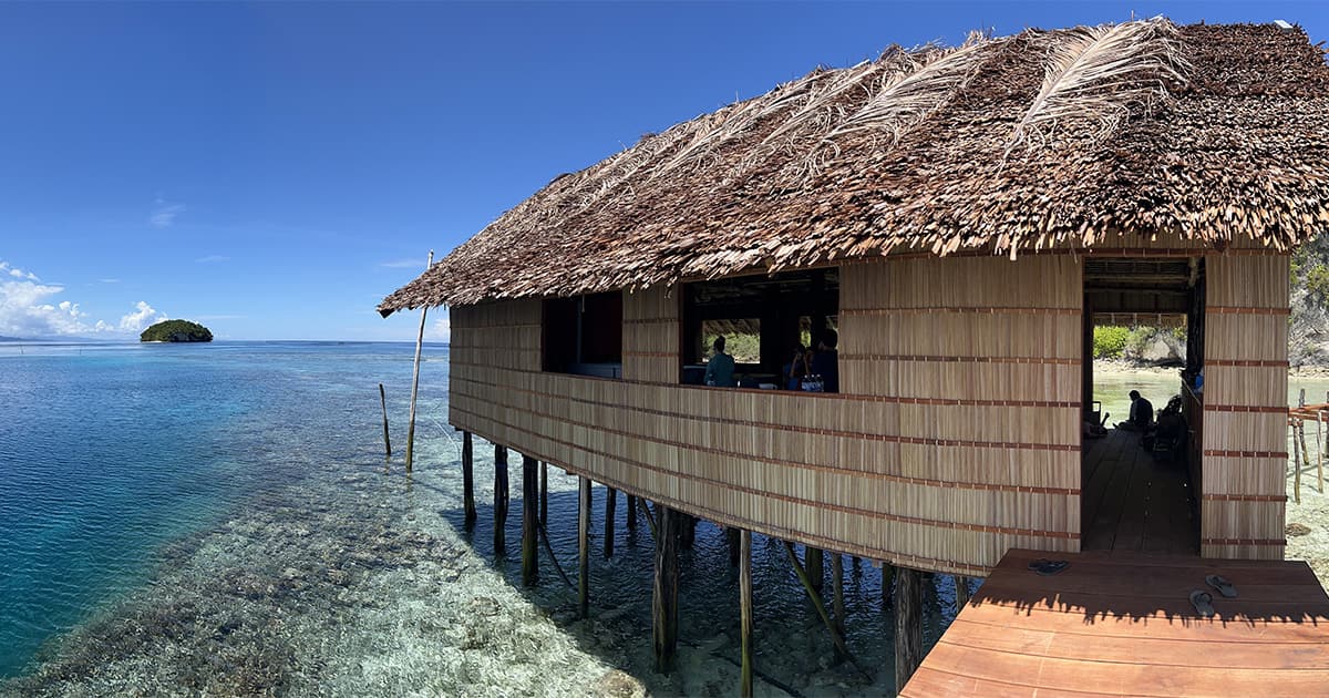 A thatched hut built on stilts over shallow water along an ocean coastline in Indonesia.