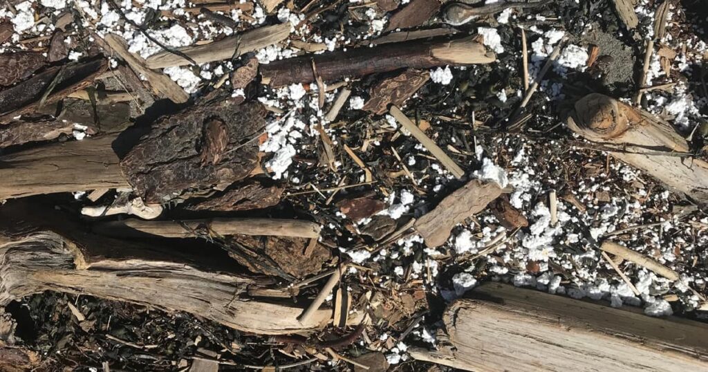 Small pieces of plastic foam packaging mixed in with rocks and pieces of driftwood on a beach.