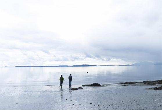 Two silhouetted figures walking along the shore of the Washington coast.
