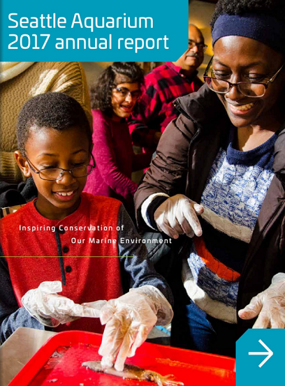 A photo of a mother and son wearing gloves and interacting with a small fish. Text in the top left corner reads "Seattle Aquarium 2017 annual report." Text in the middle of the image reads "Inspiring Conservation of Our Marine Environment."