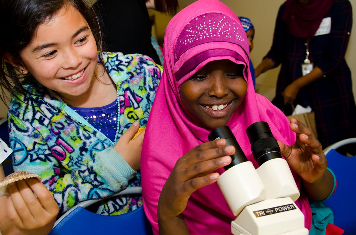 Two young girls looking through a microscope and smilling.