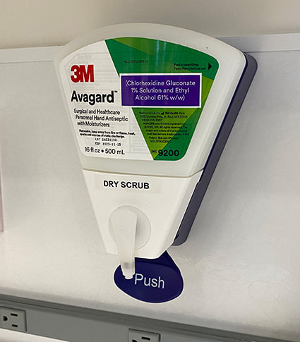 3M Avagard dry scrub dispenser attached to a wall with a push label underneath.