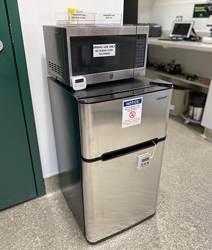 A mini fridge on the floor of a bright room with a microwave on top of it.