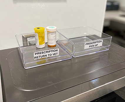 Two small plastic bins next to each other, one is labeled prescription return to vet, the other labeled prescription pick-up.
