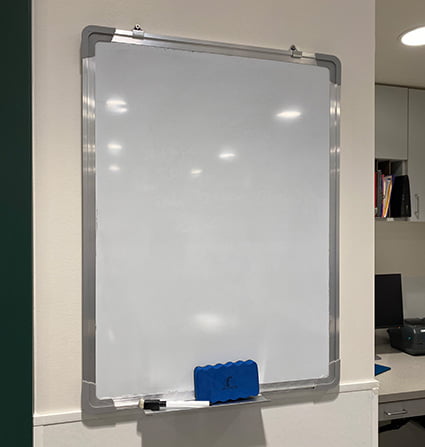 A whiteboard hanging on a wall with a marker and eraser in a tray attached to the bottom.