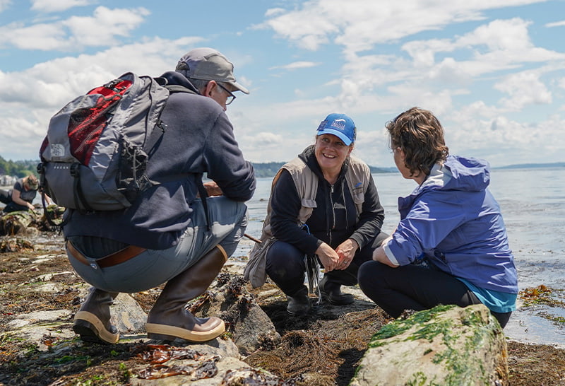 A Seattle Aquarium beach naturalist volunteer speaking to two individuals on a public beach near Seattle.