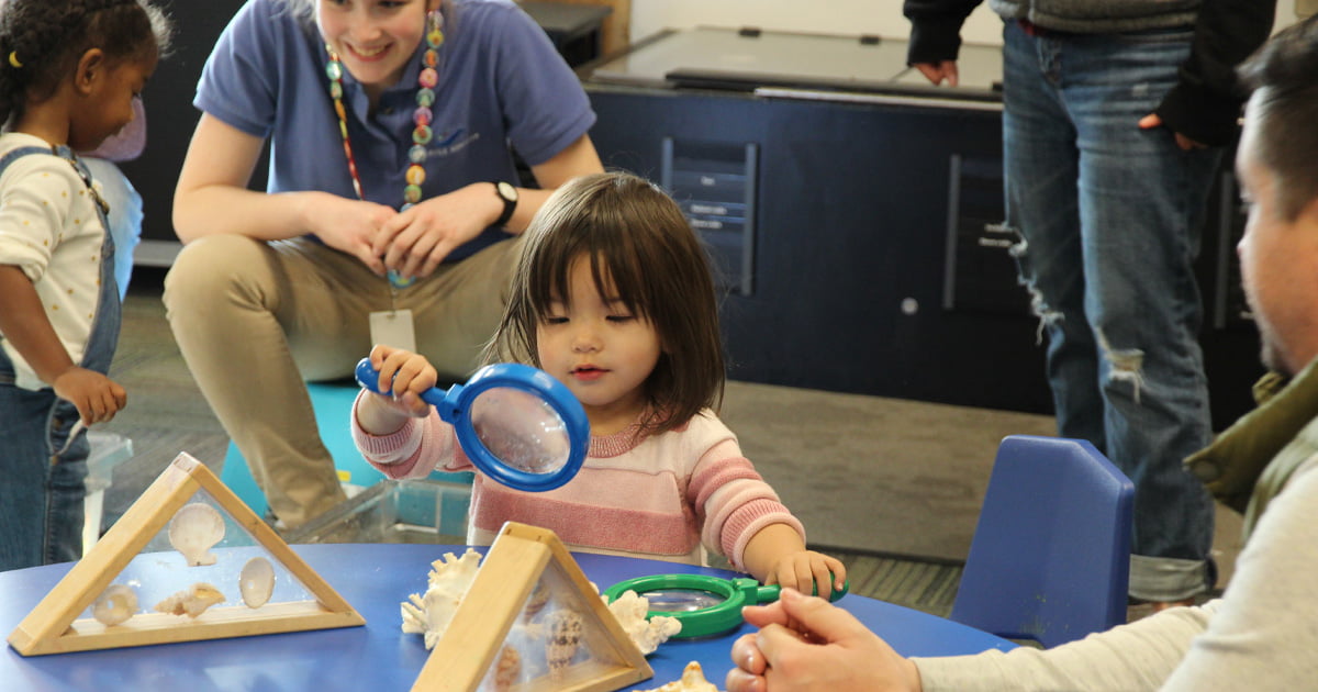 A child sitting at a table holding a large toy magnifying glass.