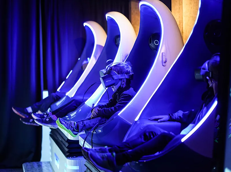 A child and other individuals sitting inside large pod shaped chairs while wearing virtual reality headsets while taking part of the VR experience at the Seattle Aquarium.