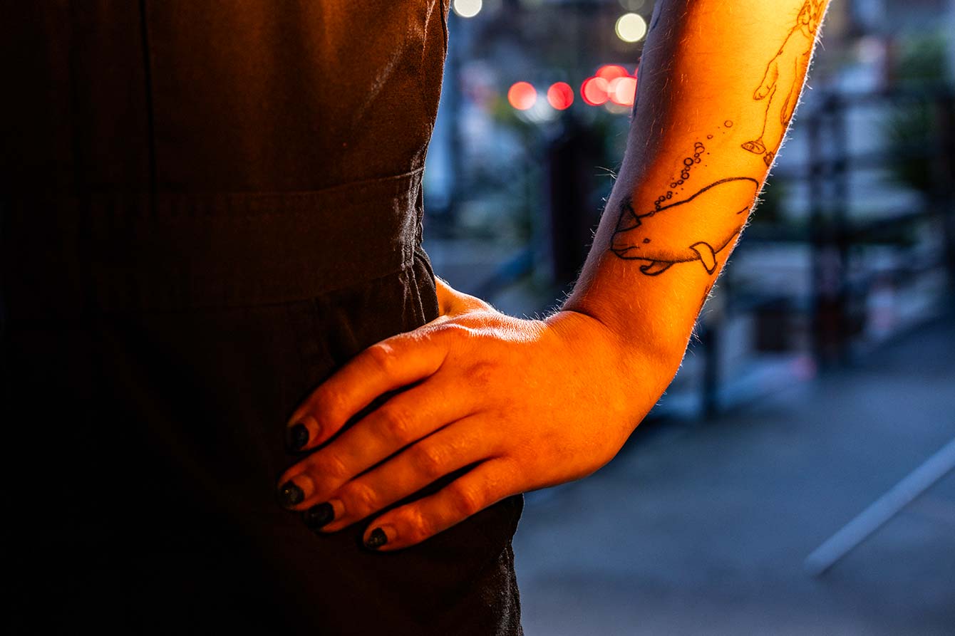 A close-up of Ben's tattoo on their left forearm, near their wrist. The tattoo is a beluga whale wearing a cone-shaped party hat; bubbles are streaming away from the whale's blowhole.