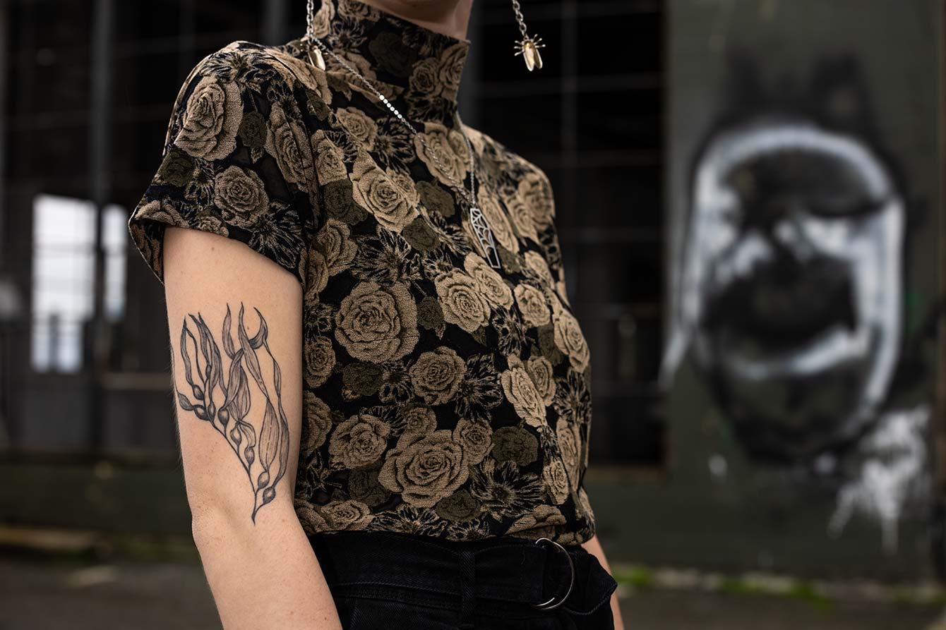 A close-up of Emma's tattoo: a monochromatic bull kelp on their upper arm.