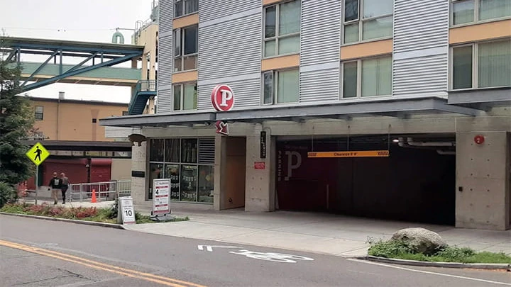 The 1901 Western Avenue entrance to the Pike Place Market Garage. A grey apartment building sits atop it, and the garage entrance is denoted by a red sign with a P on it.