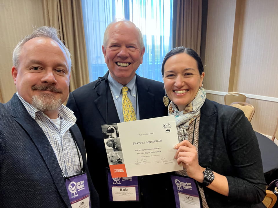 Jim Wharton, Bob Davidson, and Erin Meyer smiling while holding the Seattle Aquarium's AZA accreditation certificate.