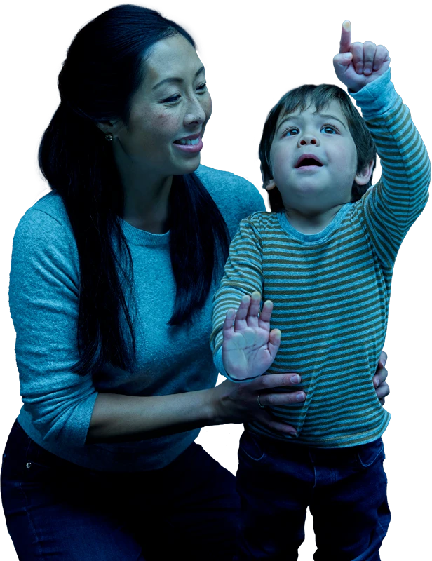 A small child pointing up as his mother holds onto his waste.