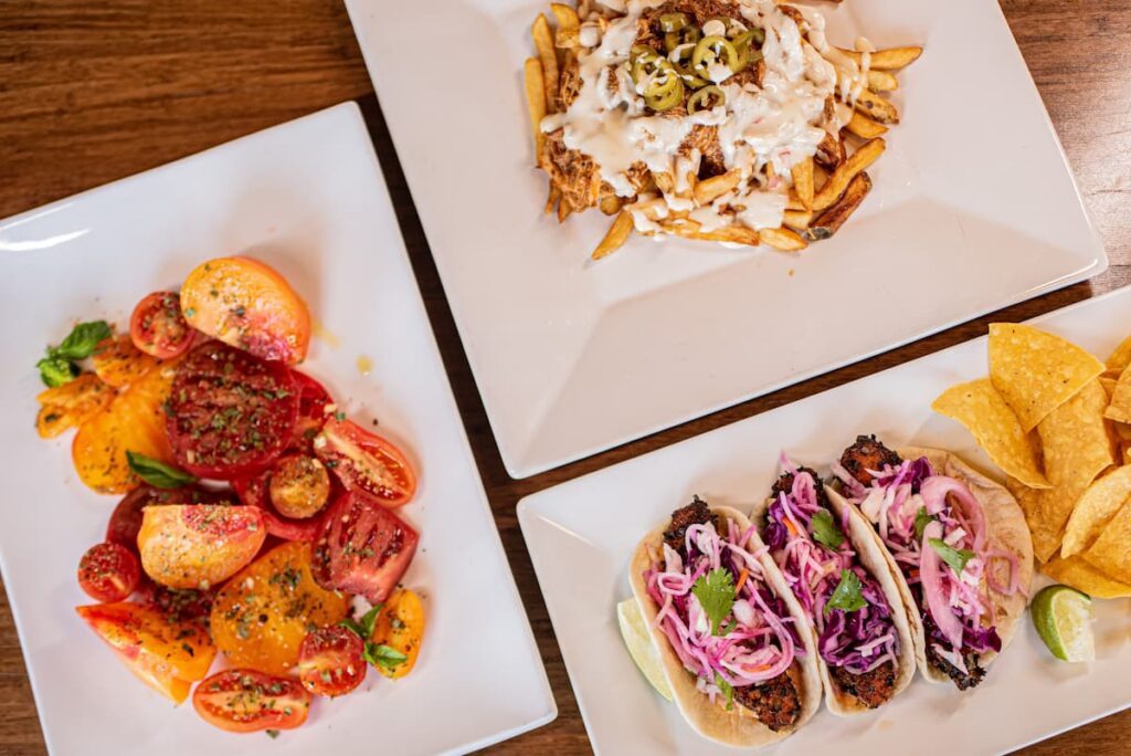Three plates of food featuring tacos and chips, roasted tomatoes, and animal-style fries.