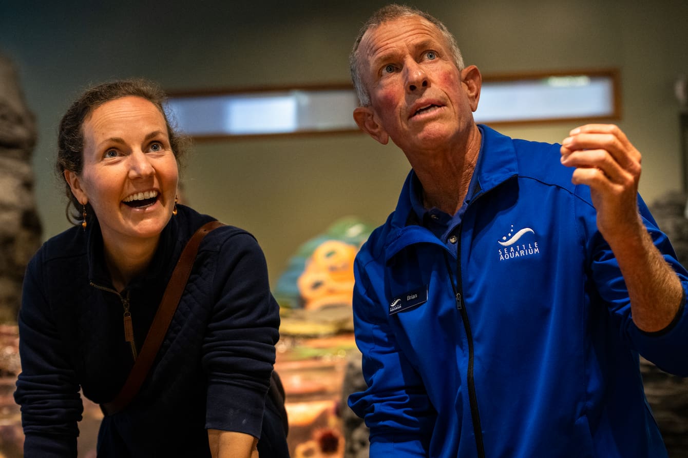 An Aquarium volunteer chatting with a smiling teacher.