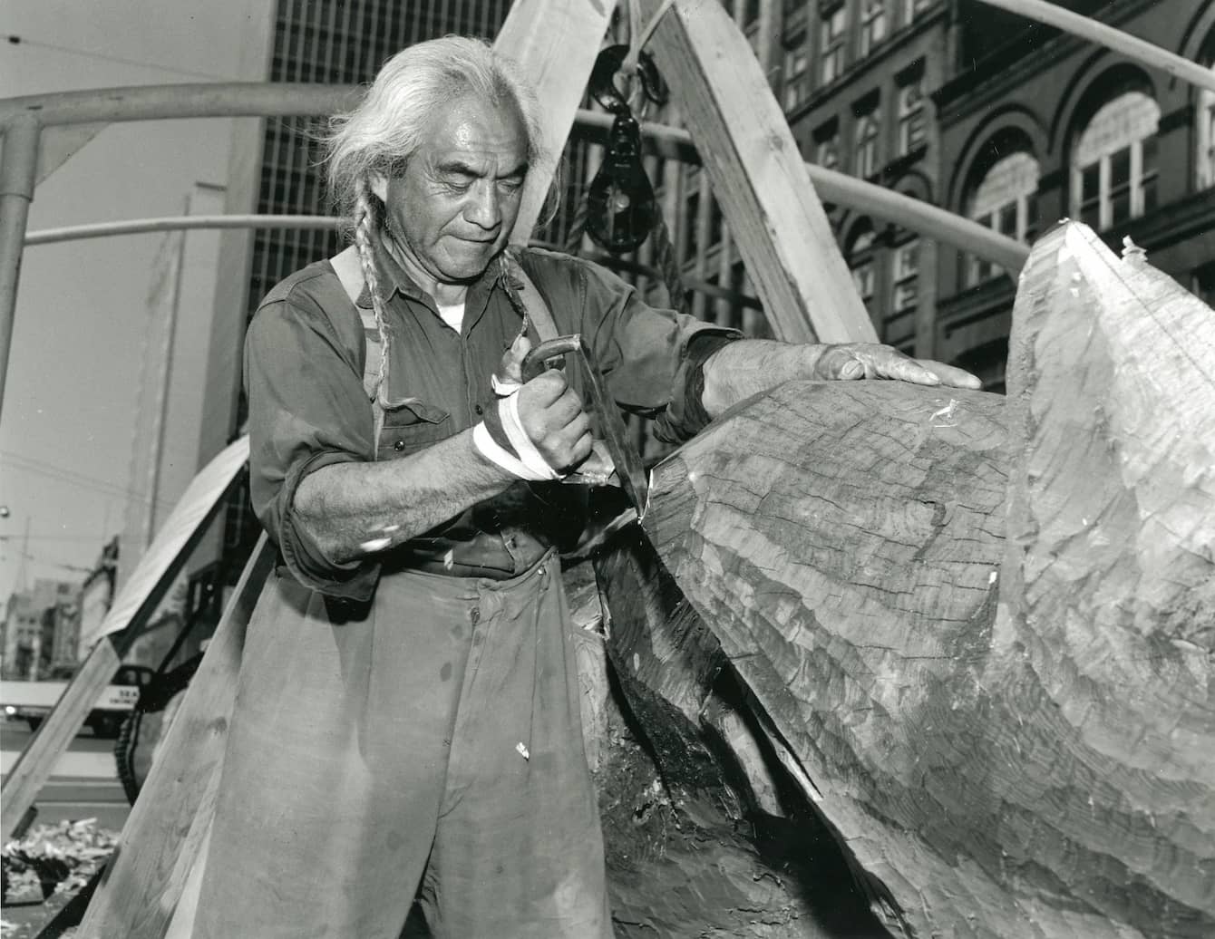 A black and white photo of Joseph Hillaire carving a wooden pole.