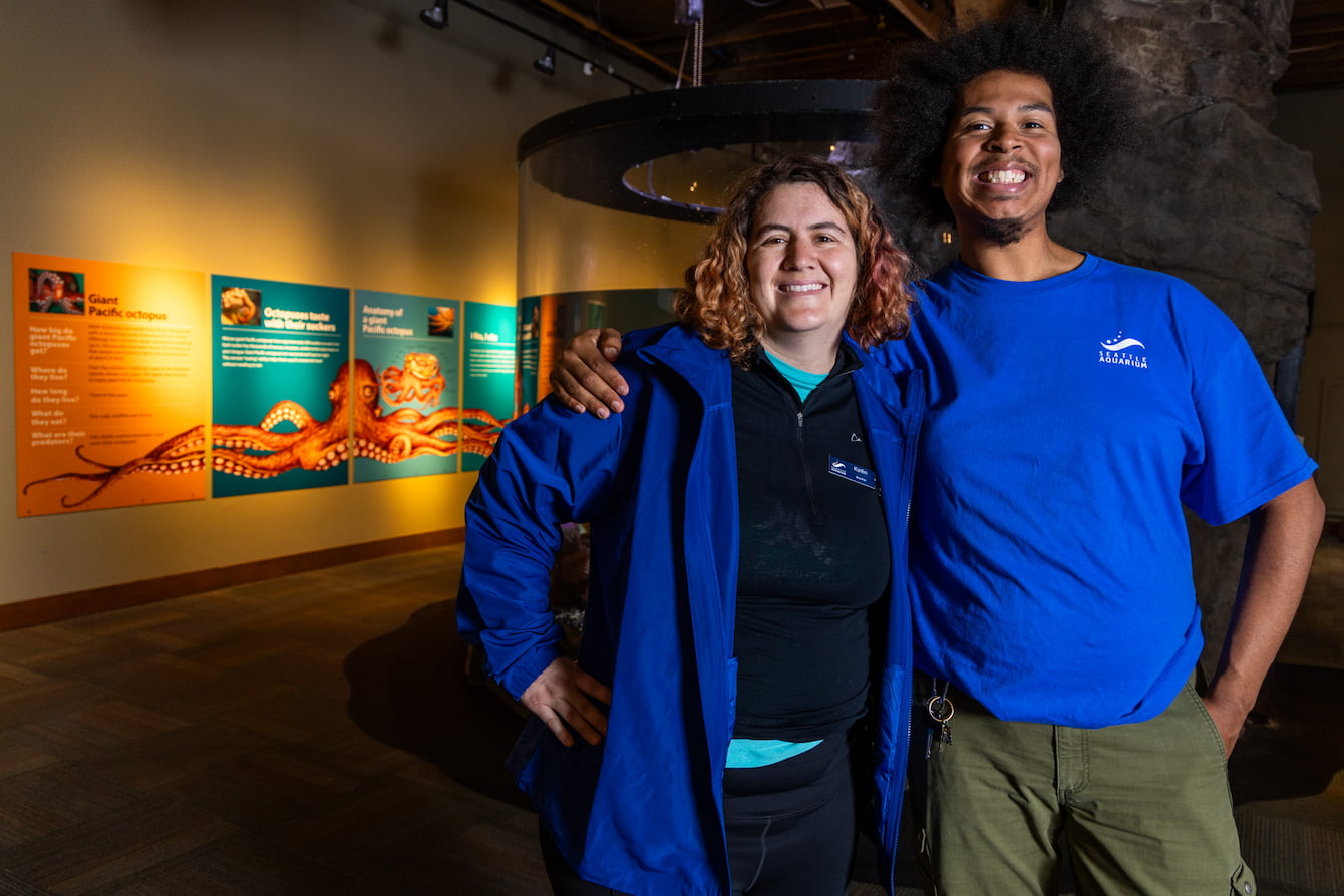 Malik Johnson and Kaitlin Brawley standing in front of the Aquarium's octopus habitat with their arms around each other's shoulders.