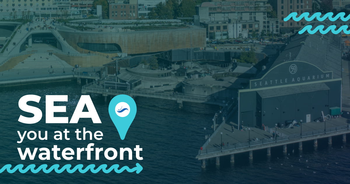 The Seattle Aquarium as seen from Elliott Bay. "SEA you at the waterfront" is written in the bottom right with a blue wave.