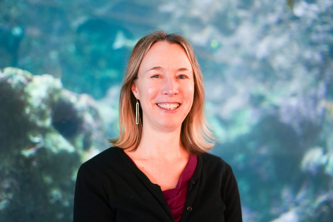 Darcie Larson, a woman with shoulder-length blonde hair, standing in front of the Window on Washington Waters habitat.