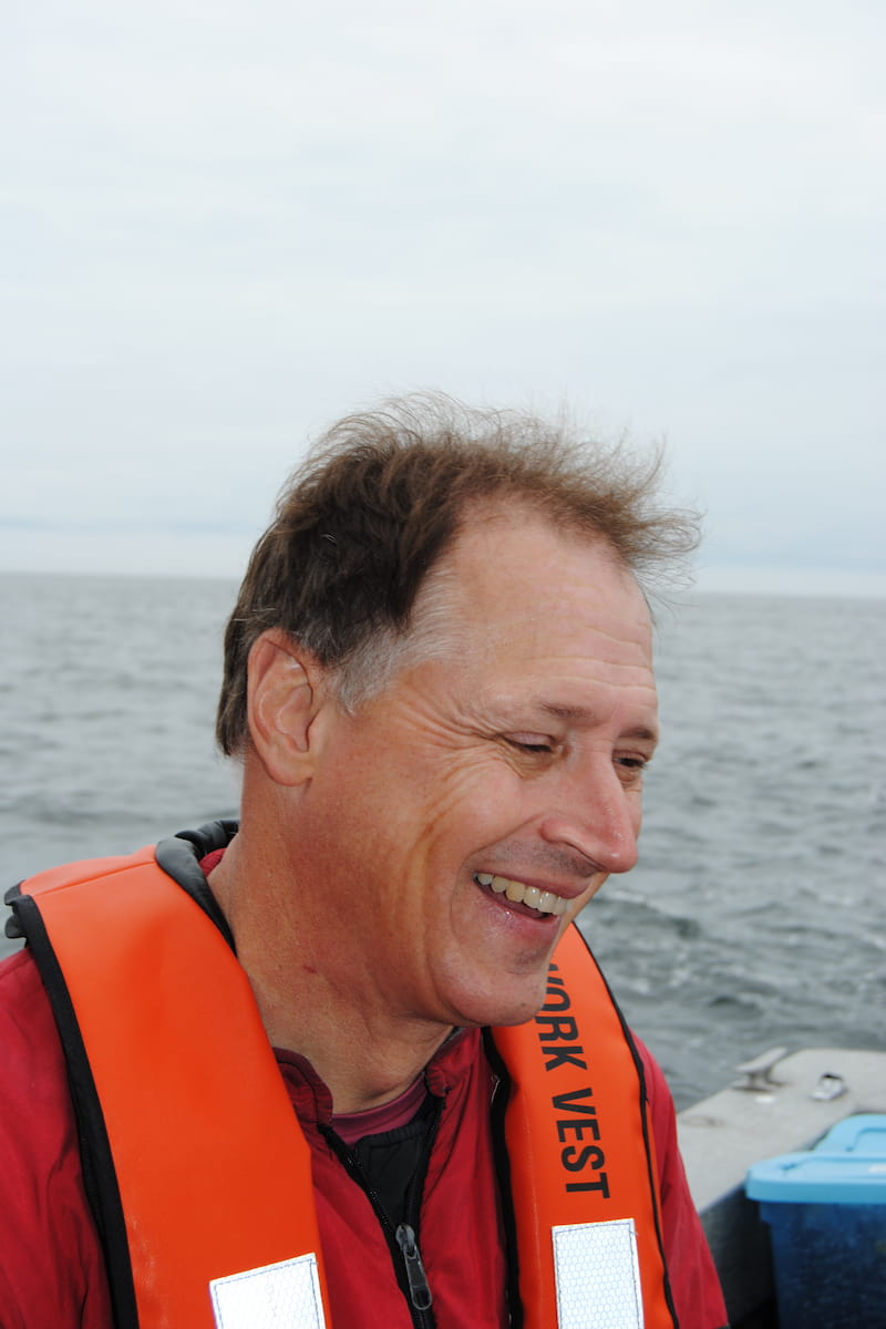 Jeff smiling. He is on a boat on the sea and is wearing an orange work vest.