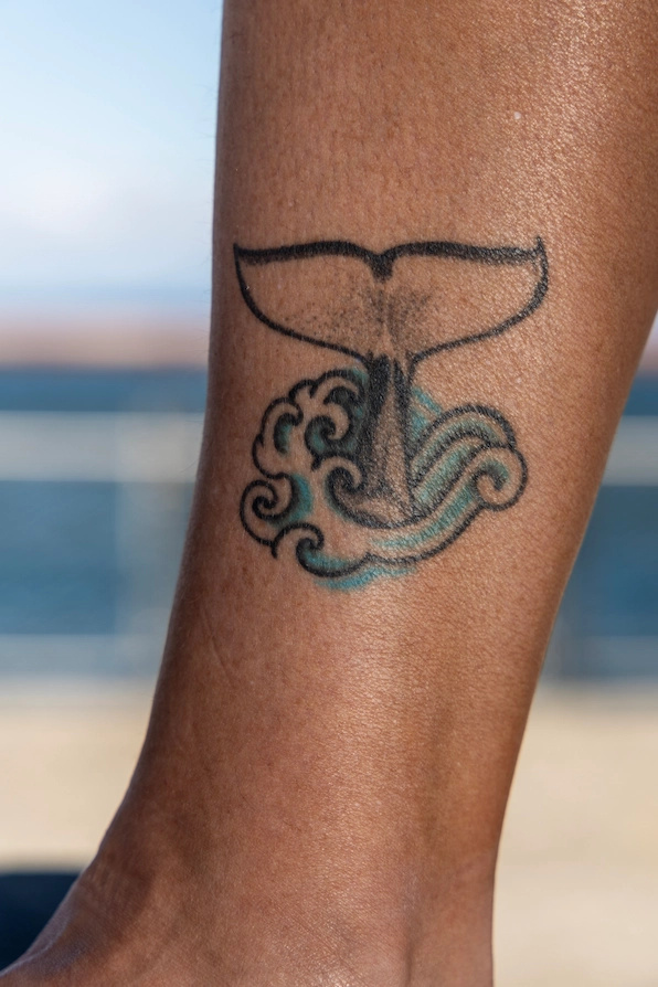 Taylor's tattoo of a whale's tail above the surface of a wave. The tattoo is located on her inner ankle.