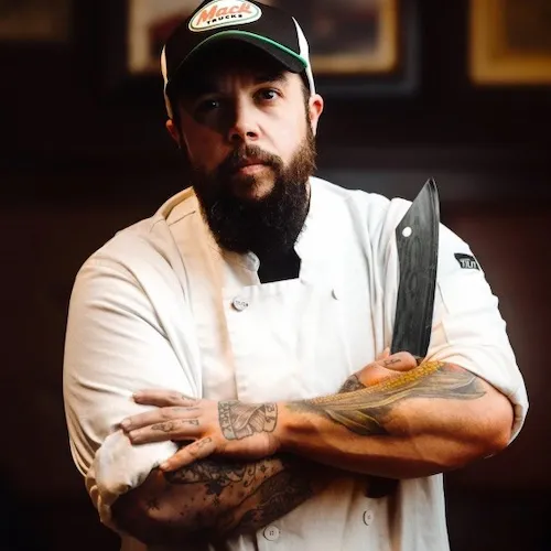 Chef Finnley Nash posing for a photo, arms crossed, holding a chef's knife in the right hand.
