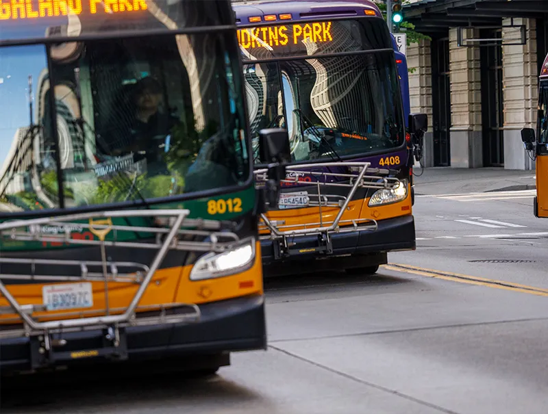 Two King County Metro public transit buses driving down a street in Seattle next to one another, traveling in the same direction.