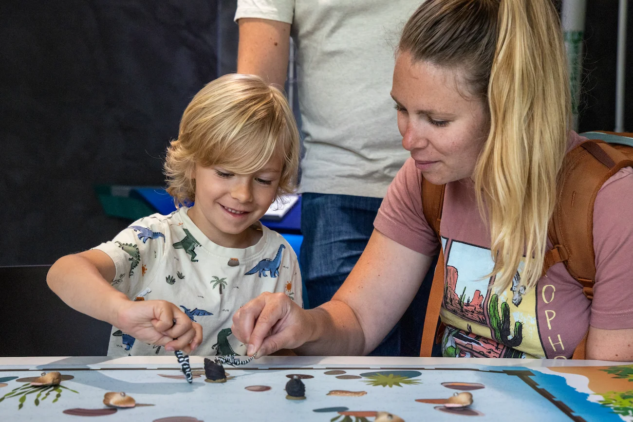 An adult woman and a young child holding small plastic shark figures while participating in an learning activity at the Seattle Aquarium's Discovery Lab.